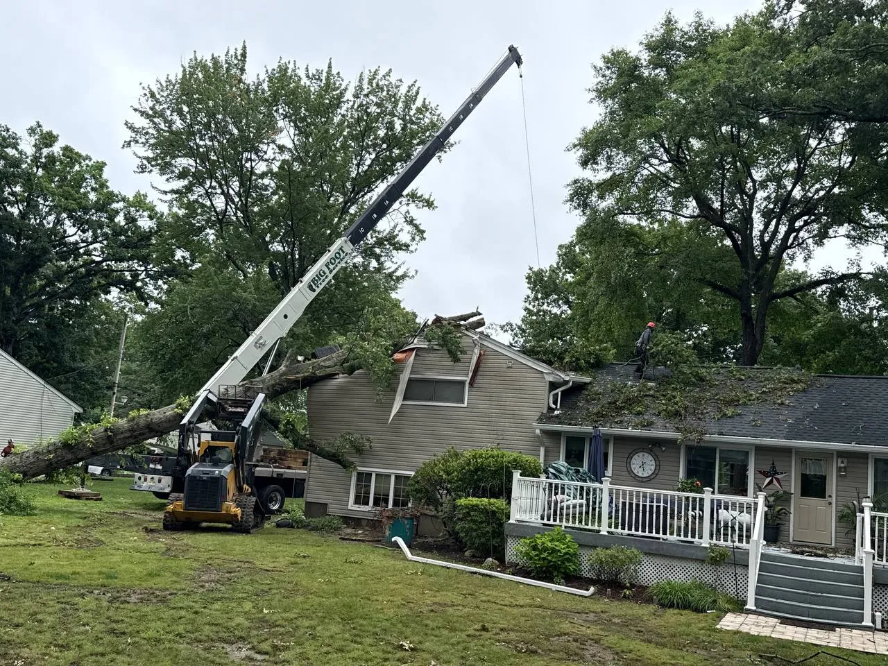 Crane removing tree from house after storm